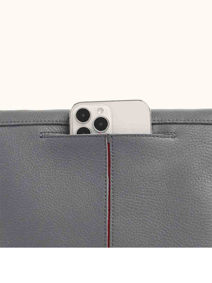 A smartphone peeks out from the top pocket of a Hammitt Los Angeles VIP Medium Clutch in Sonnet Grey, crafted from chic pebbled leather.