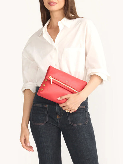 A person in a white shirt and jeans holds a Hammitt Los Angeles VIP Medium Clutch in Poppy Red with gold zipper details.