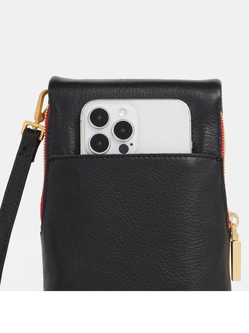 The Hammitt Los Angeles VIP Mobile in Black features a pebbled leather exterior with a brushed gold and red zip. It has a white smartphone partially visible in the front pocket and is designed as a chic crossbody bag, complete with a detachable strap for versatile styling.