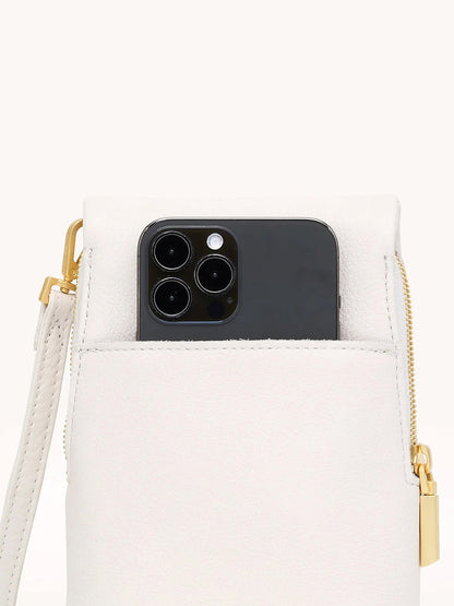 A black smartphone is partially inserted into the front pocket of the Hammitt Los Angeles VIP Mobile in Calla Lily White/Brushed Gold, featuring pebble leather with a gold zipper and wrist strap, ideal for your crossbody bag.