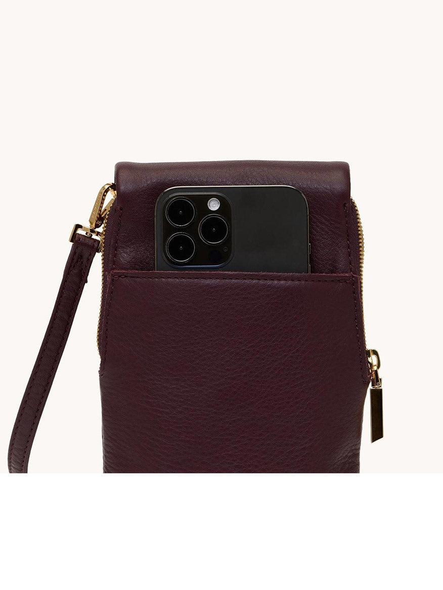 The Hammitt Los Angeles VIP Mobile in Regatta Stripe/Gold, with a wrist strap and crossbody style, holds a black smartphone partly tucked into its front pocket, showcasing the device's camera lenses.