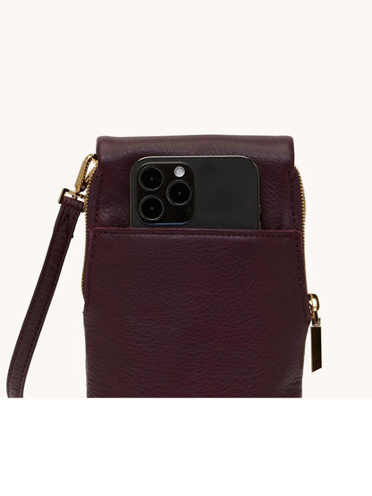 The Hammitt Los Angeles VIP Mobile in Regatta Stripe/Gold, with a wrist strap and crossbody style, holds a black smartphone partly tucked into its front pocket, showcasing the device's camera lenses.