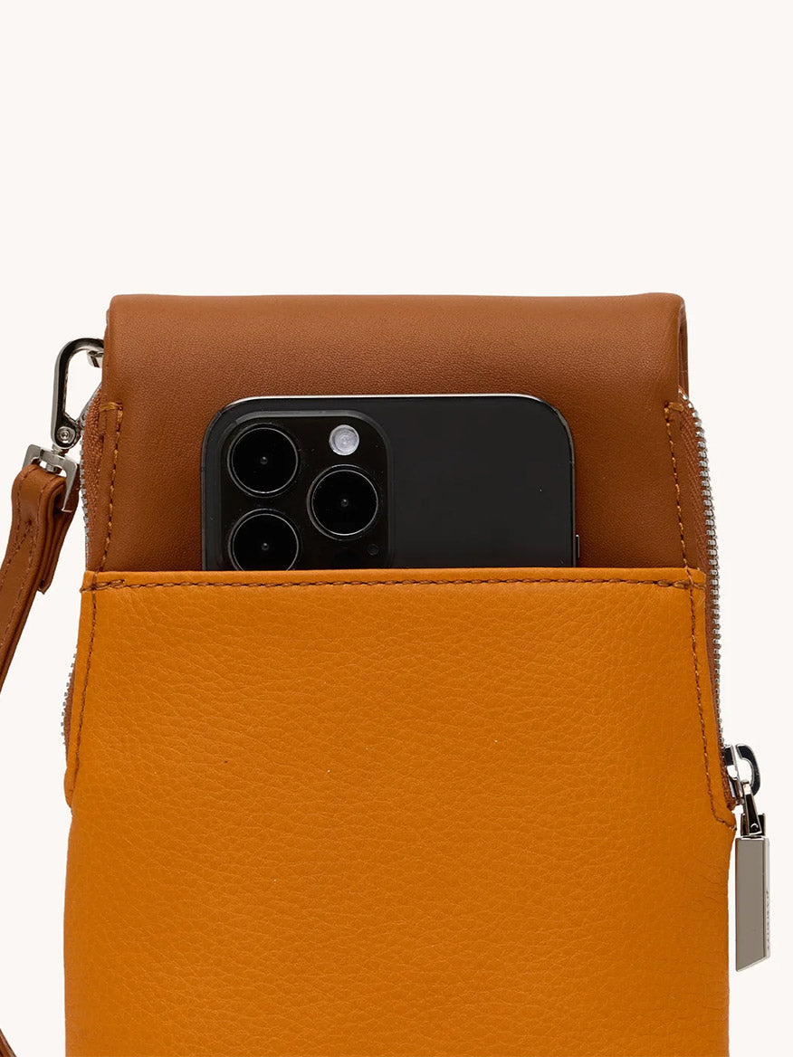 A black smartphone peeks from the front pocket of the Hammitt Los Angeles VIP Mobile in Tailored Tangerine/Silver, highlighting its clever cellphone pocket handbag design with a zipper and strap.