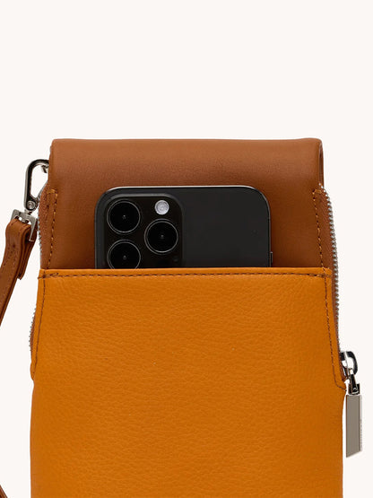 A black smartphone peeks from the front pocket of the Hammitt Los Angeles VIP Mobile in Tailored Tangerine/Silver, highlighting its clever cellphone pocket handbag design with a zipper and strap.