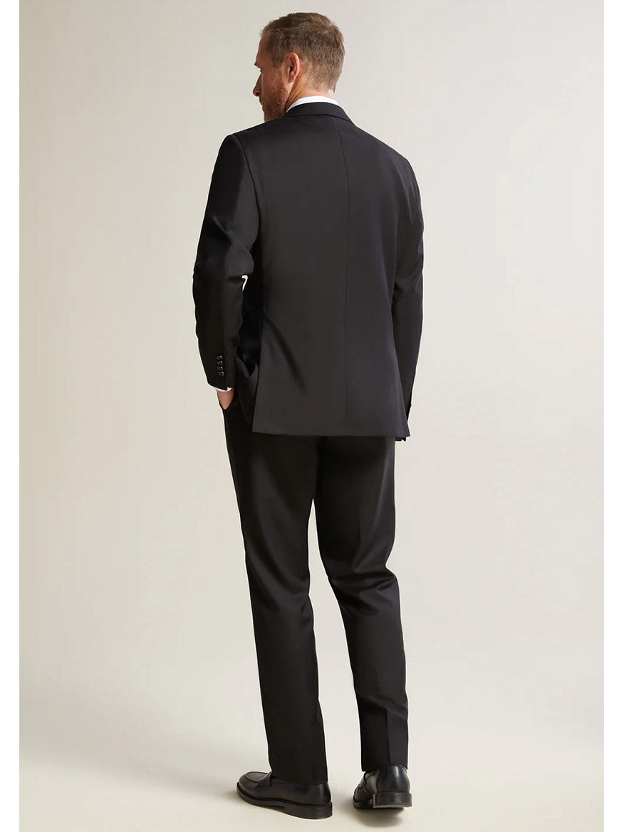 A man in a Hickey Freeman (Heritage Gold) Black Infinity Suit stands facing away, highlighting the back of his jacket and pants made from luxurious Super 140s Infinity wool by the renowned Carlo Barbera mill.