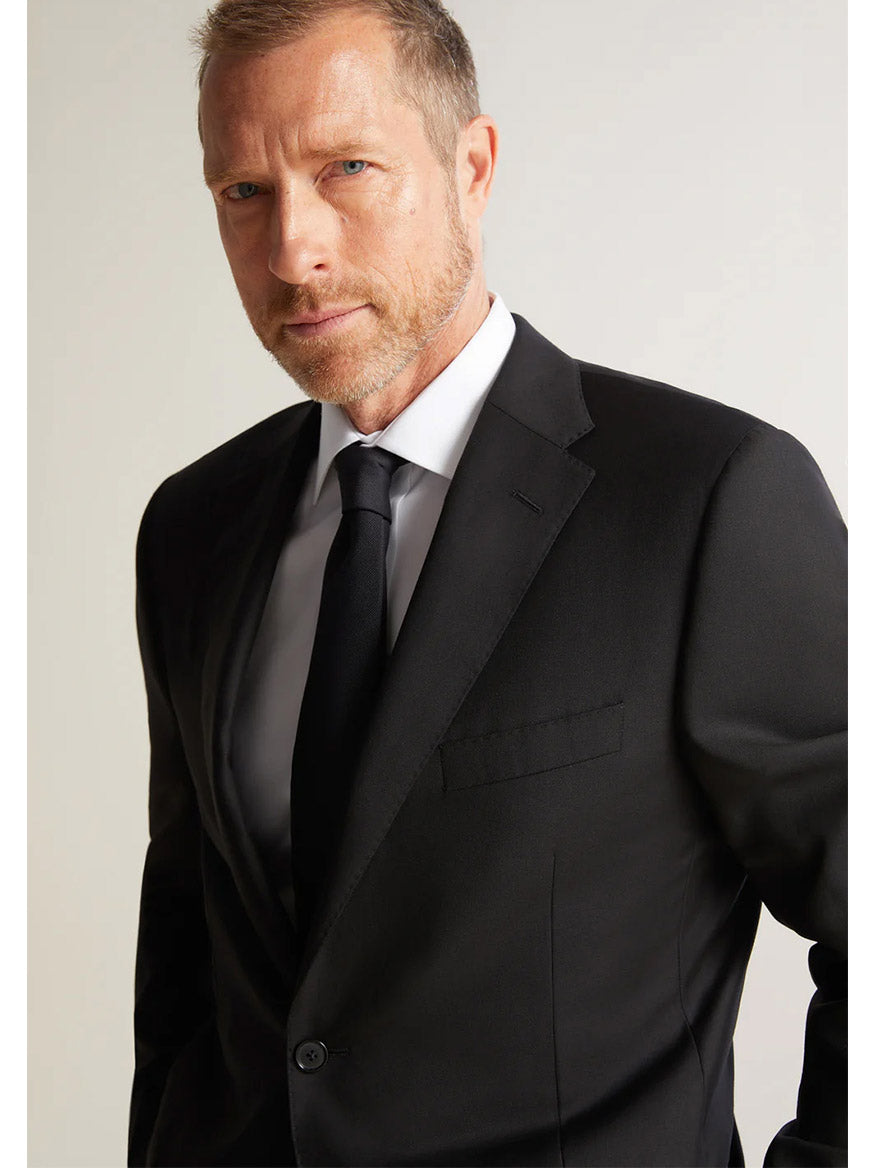 A man with a beard wearing the Hickey Freeman (Heritage Gold) Black Infinity Suit, crafted from Super 140s Infinity wool by the Carlo Barbera mill, gazes confidently towards the camera.