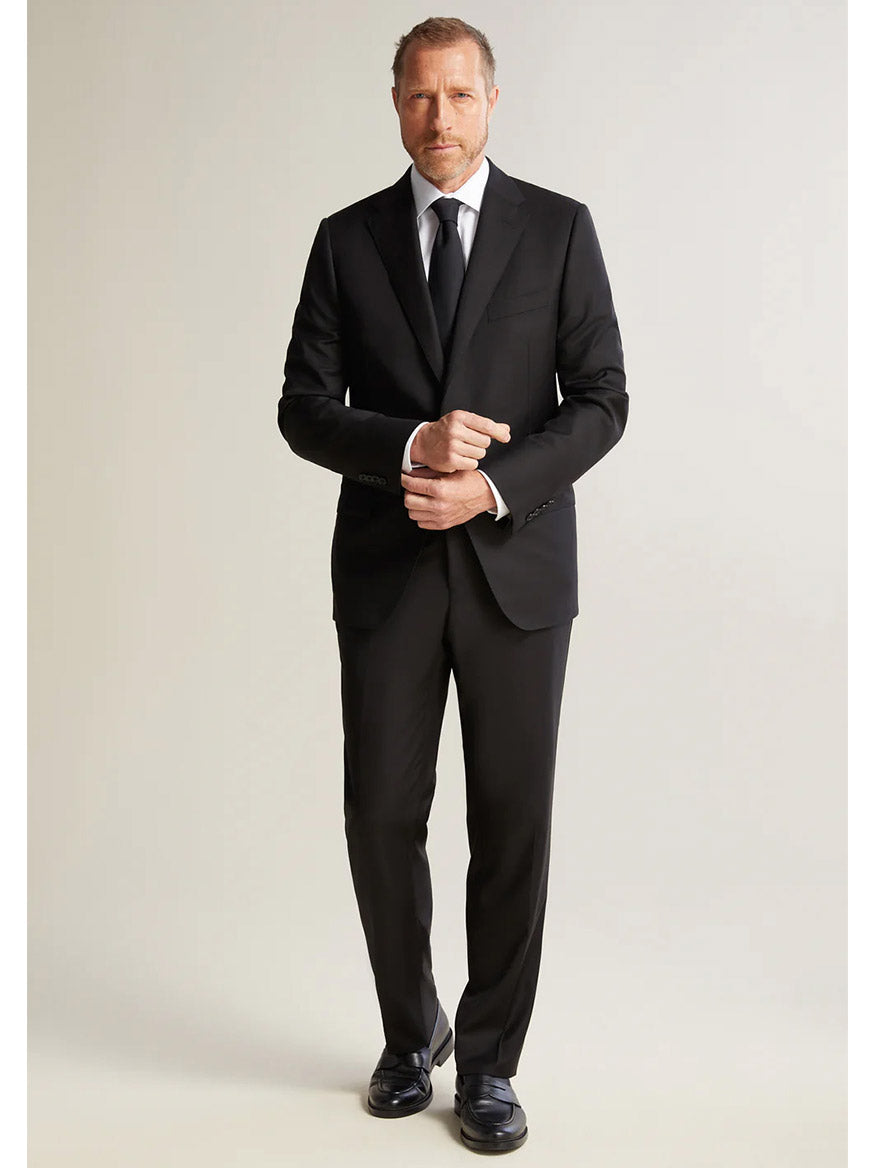 A man wearing the Hickey Freeman (Heritage Gold) Black Infinity Suit, made from Super 140s wool, stands against a neutral background, adjusting his sleeve.