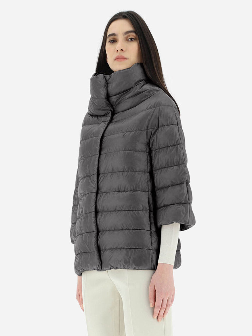 A woman in a Herno Aminta 3/4 Sleeve Cocoon Jacket in Anthracite with goose down padding and white trousers stands against a plain background.