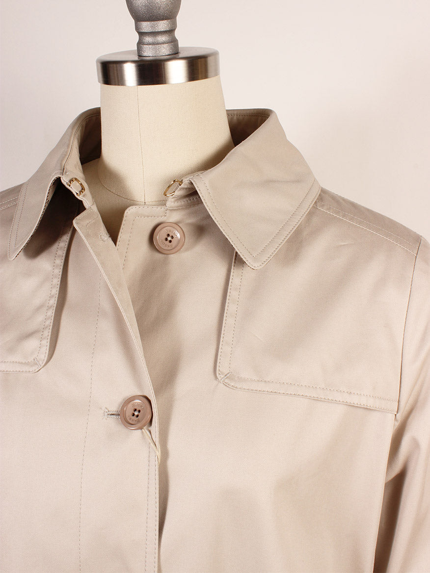 The Herno Delon and Monogram Trench Coat in Champagne is displayed on a mannequin, made from cotton gabardine with a collared neckline and two buttons. Its water-repellent coating makes it perfect for unpredictable weather.