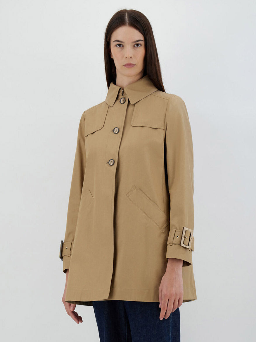 A woman stands against a plain background wearing a stylish Herno Delon and Monogram Trench Coat in Sabbia with large buttons and buckle details at the cuffs, crafted from cotton gabardine.