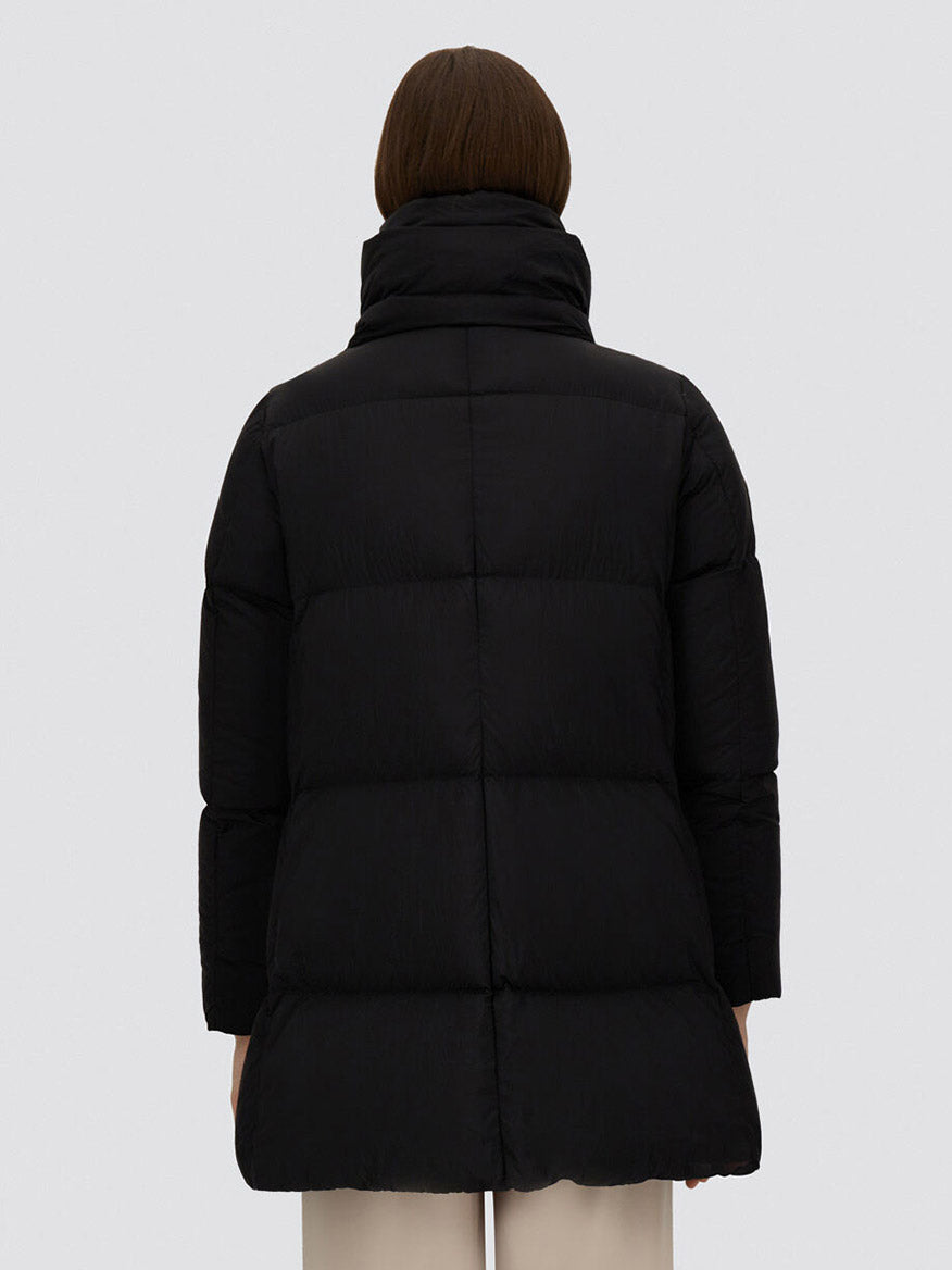 A person with short brown hair is seen from the back, wearing the black Herno A-Shape Jacket in Ecoage and beige pants, set against a plain light background.