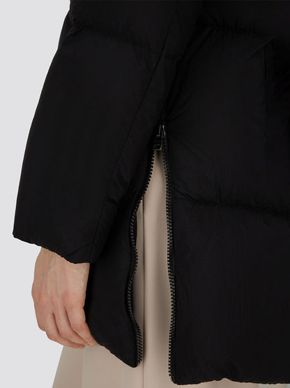 A close-up of a hand next to the side zipper of the Herno A-Shape Jacket in Ecoage in Black, made from recycled nylon with goose down padding, with a beige garment partially visible underneath.