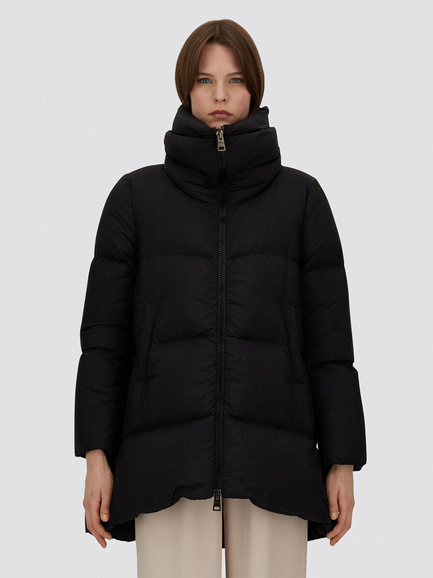 A person stands facing forward wearing the Herno A-Shape Jacket in Ecoage in Black and beige pants against a plain light gray background.