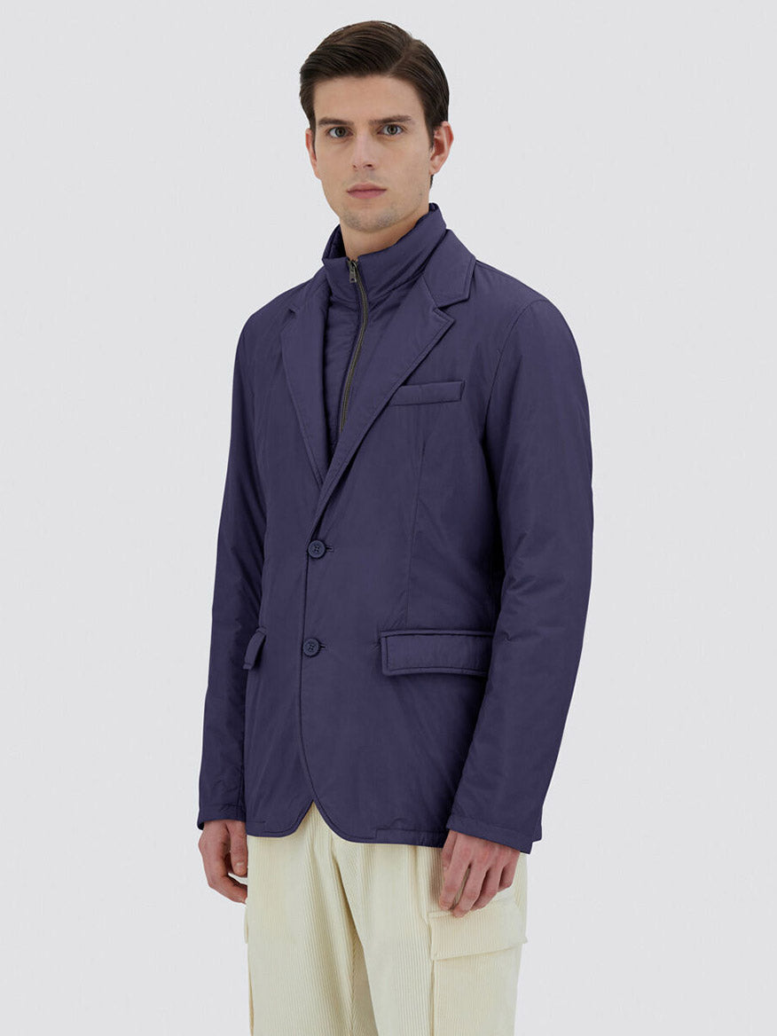 A person wearing a tailored-style outfit featuring the Herno Blazer in Ecoage in New Blue over a zippered top and light-colored pants, crafted from recycled nylon microfibre, stands against a plain background.