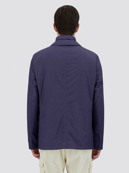 A person wearing the Herno Blazer in Ecoage in New Blue, designed in a tailored style from recycled nylon microfiber, paired with light-colored pants is shown from the back against a plain background.