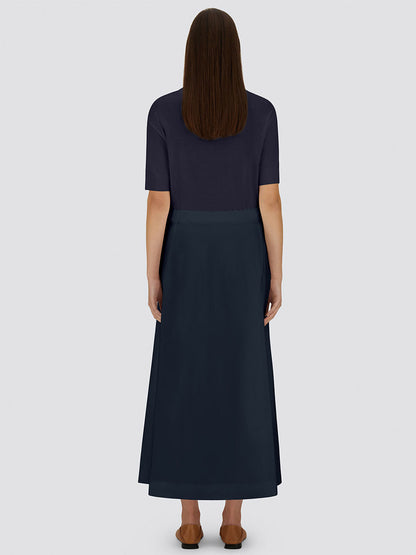 Woman standing with her back to the camera, wearing the Herno Glam Knit Effect Dress in Techno Taffeta in navy and brown shoes against a plain light gray background.