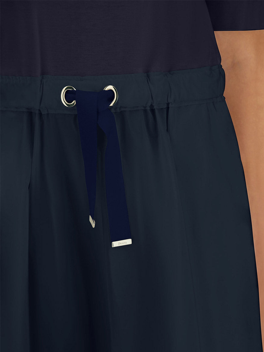 Close-up of a person wearing the Herno Glam Knit Effect Dress in techno taffeta in navy, featuring a water-repellent finish, adjustable drawstring waistband with silver grommets, and paired with a dark top.