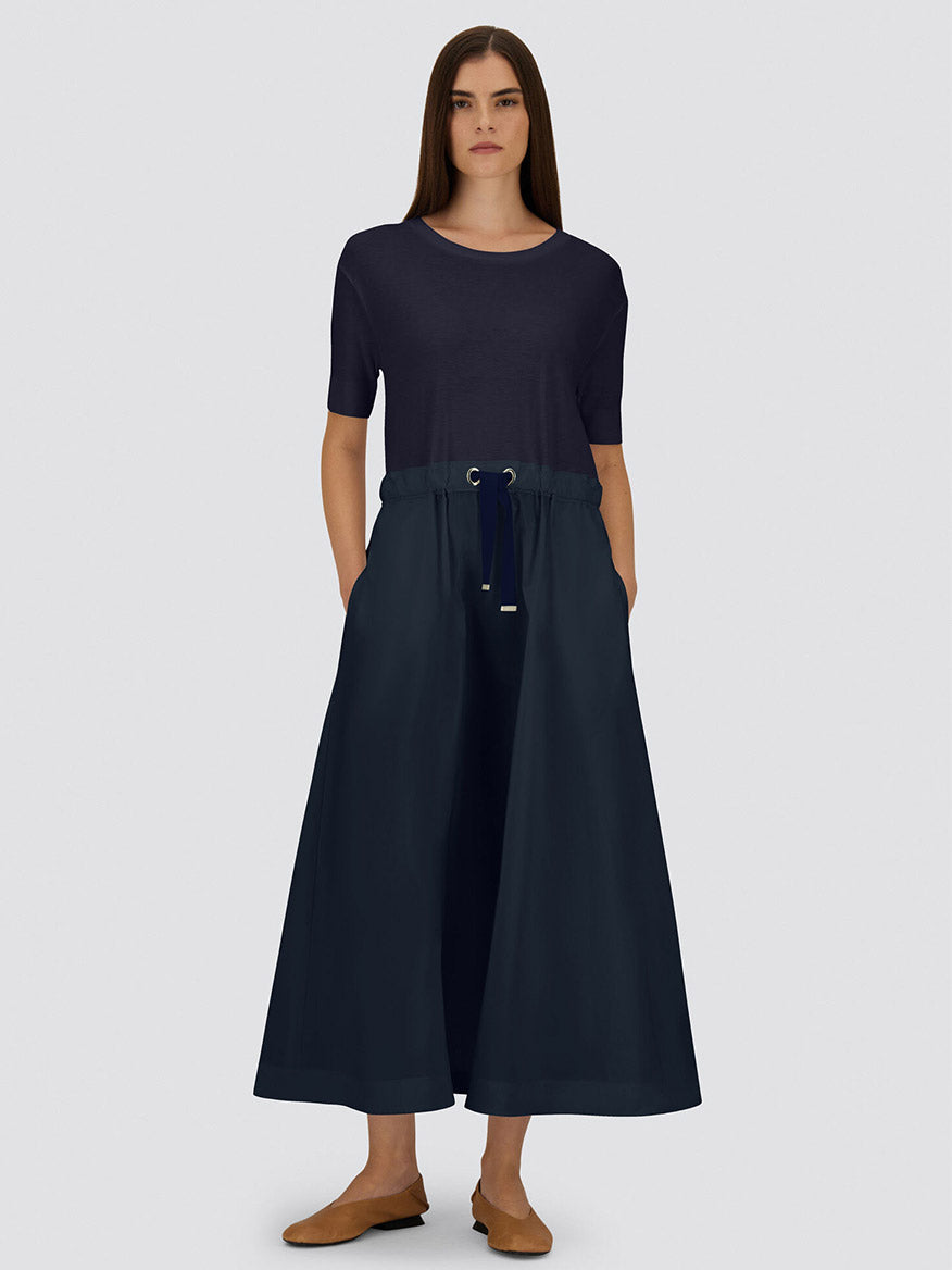 A woman faces forward wearing the Herno Glam Knit Effect Dress in Techno Taffeta in Navy, styled with brown flat shoes against a plain light gray background.