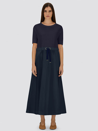 A woman stands facing forward in the Herno Glam Knit Effect Dress in Techno Taffeta in Navy, paired with brown flats, against a plain background to highlight the minimalist design.