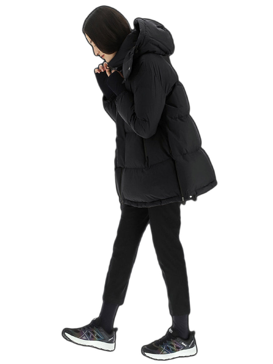 A woman in a Herno Laminar Oversize Gore-Tex Windstopper Coat in Black and pants walking to the left, zipping up her jacket, isolated on a white background.