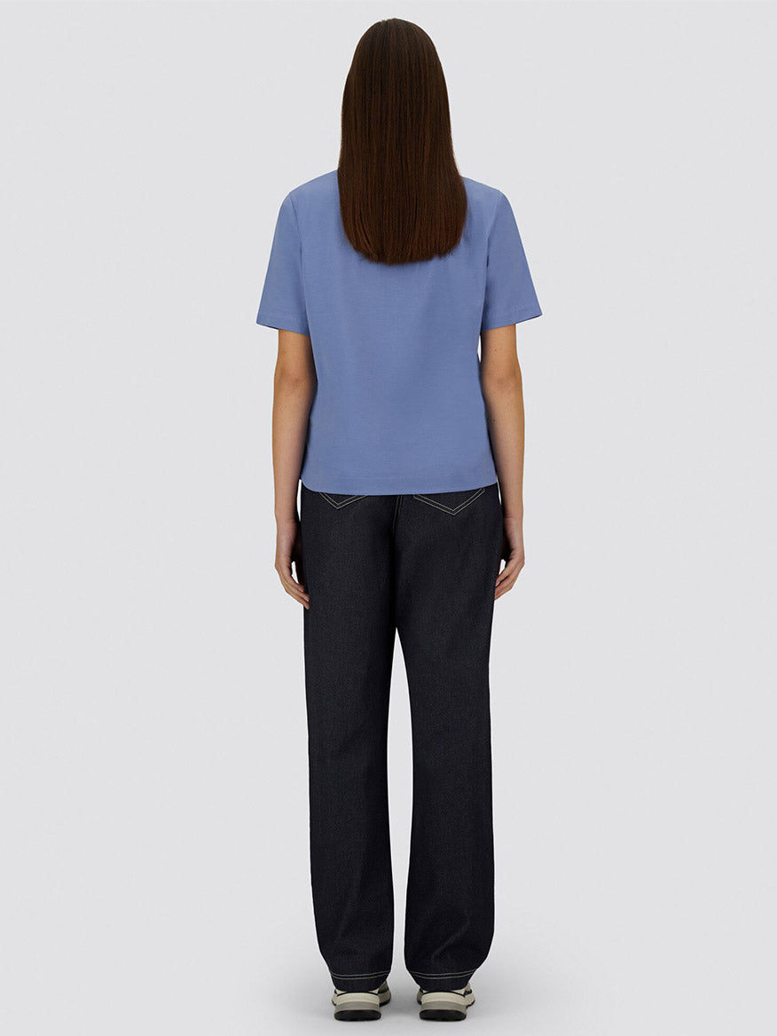 A person stands facing away, wearing the Herno Superfine Cotton Stretch T-Shirt in Light Blue, dark jeans, and sneakers against a plain gray background.