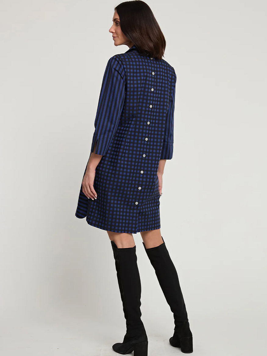 A woman wearing a Hinson Wu Aileen 3/4 Sleeve Stripe/Gingham Combo Dress in Sapphire/Black, paired with black knee-high boots, is standing and facing away from the camera.