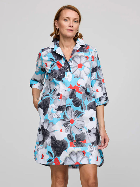 A woman stands against a plain background, left hand in her pocket, wearing the Hinson Wu Aileen 3/4 Sleeve Pop Art Flower Dress in Blue Combo—a knee-length, button-up dress featuring exclusive floral prints.