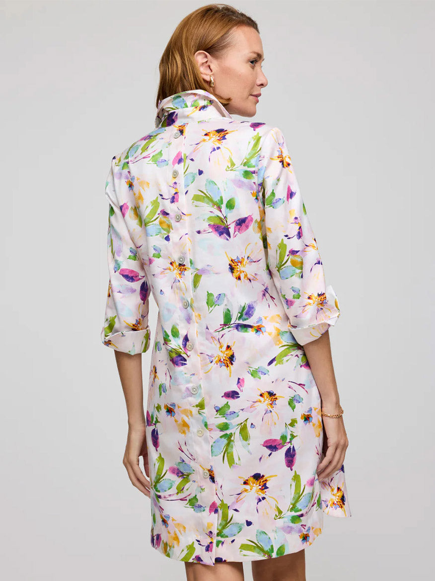 Wearing the Hinson Wu Aileen 3/4 Sleeve Garden Sateen Dress in Garden Multi, a woman faces away. Made from Cotton Blend Satin, it features a colorful floral pattern, rolled-up sleeves, back buttons, and is machine washable.