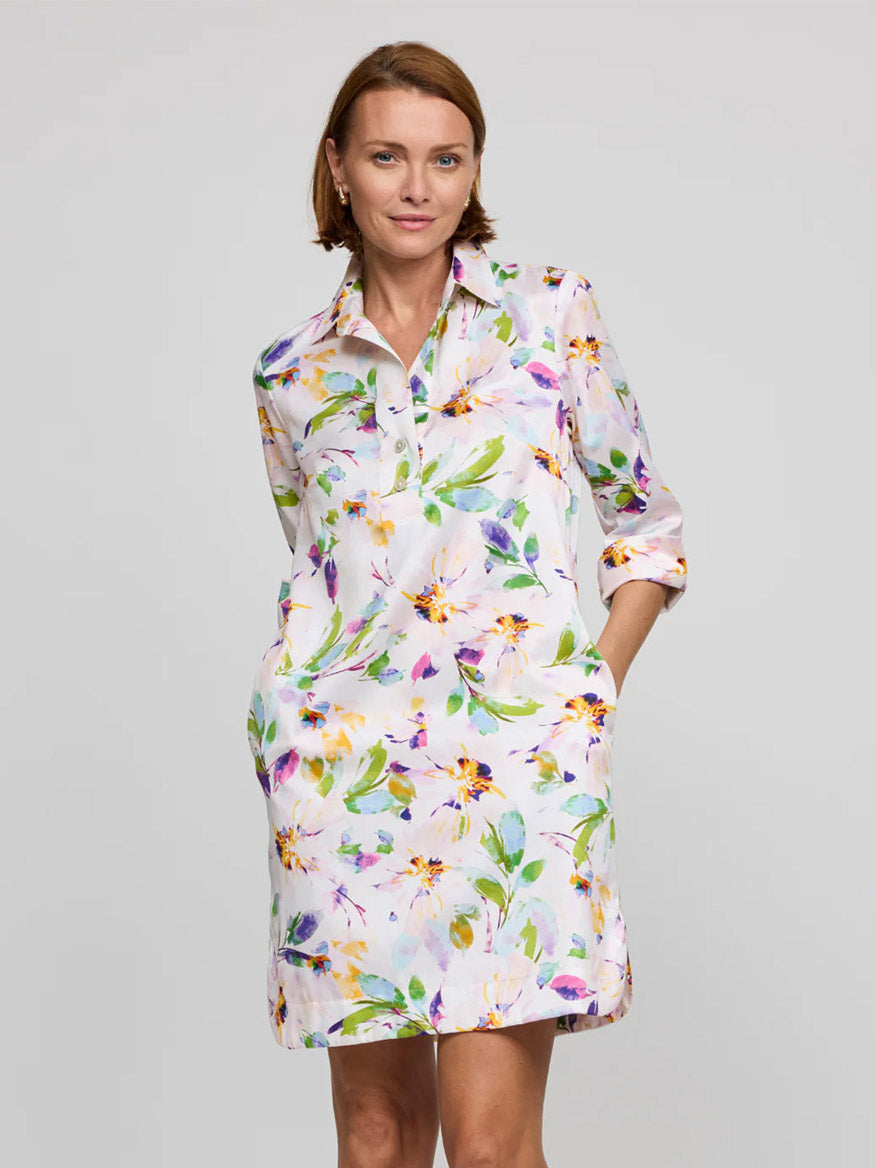 A woman wears the Hinson Wu Aileen 3/4 Sleeve Garden Sateen Dress in Garden Multi, a cotton-blend satin dress with a white base and colorful floral print, standing against a plain light gray background.