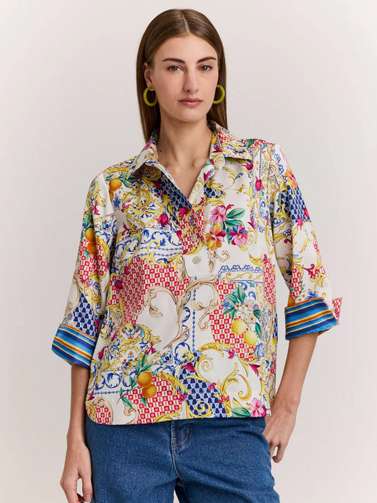 Model wears the Hinson Wu Aileen 3/4 Sleeve Amalfi Print Top—a colorful, patterned button-up in luxurious cotton blend satin with floral and geometric designs, blue striped cuffs—paired with blue jeans against a plain light background.