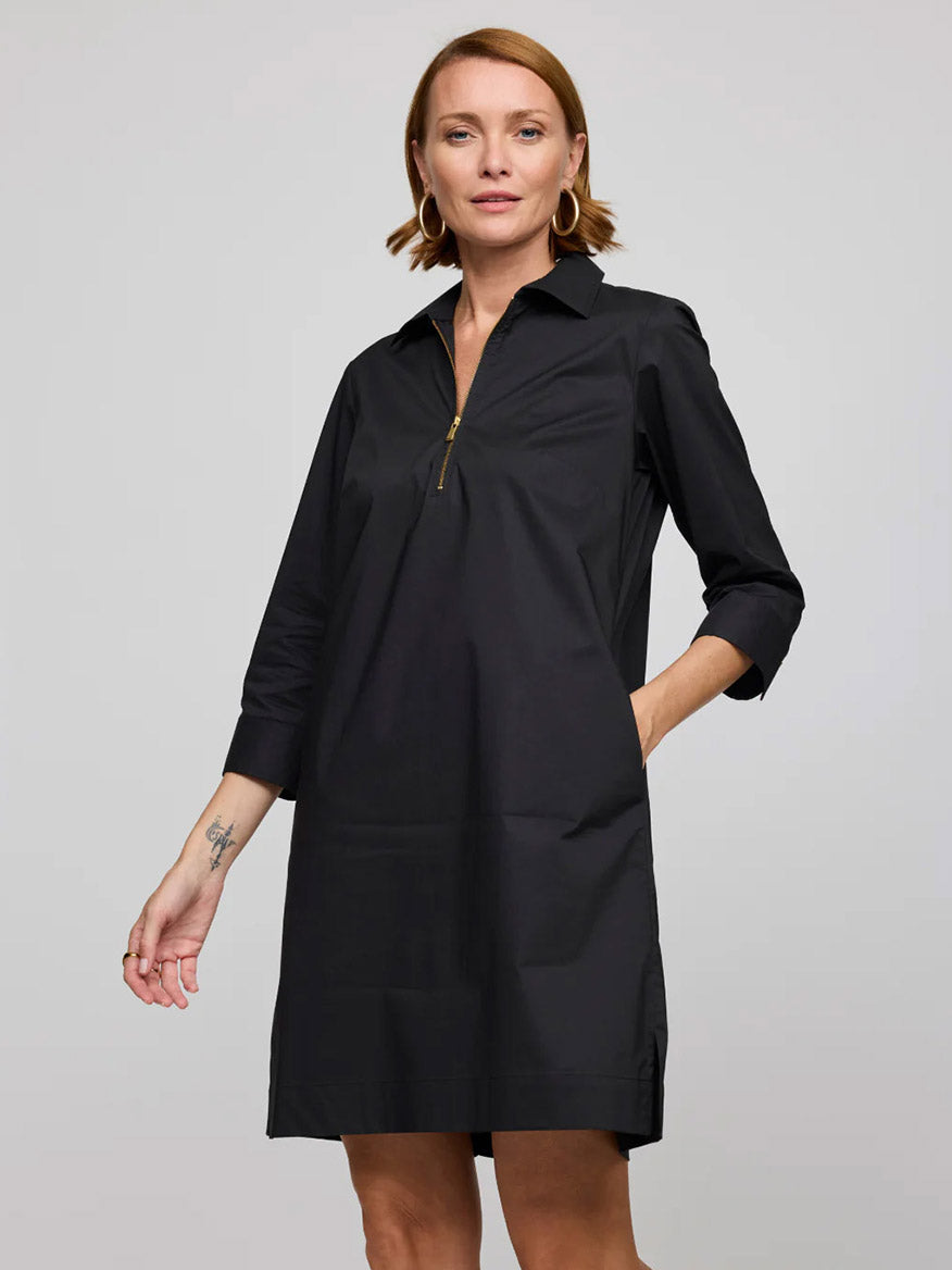 A woman wears the Hinson Wu Alessa 3/4 Sleeve Dress in Black—a knee-length, stretch polished cotton dress with a collar, front zipper, three-quarter sleeves, and pockets—standing against a plain background.