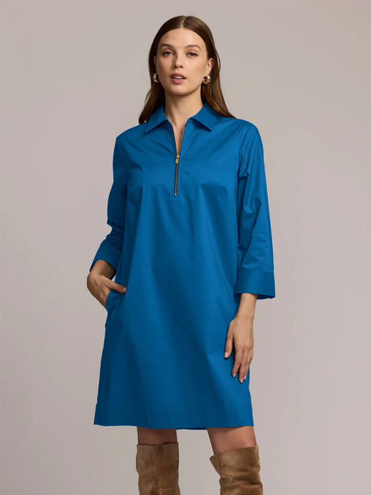 A woman stands facing forward in the Hinson Wu Alessa 3/4 Sleeve Dress in Bright Sapphire, featuring a boxy fit, blue long sleeves, and a front zipper, paired with tan knee-high boots.