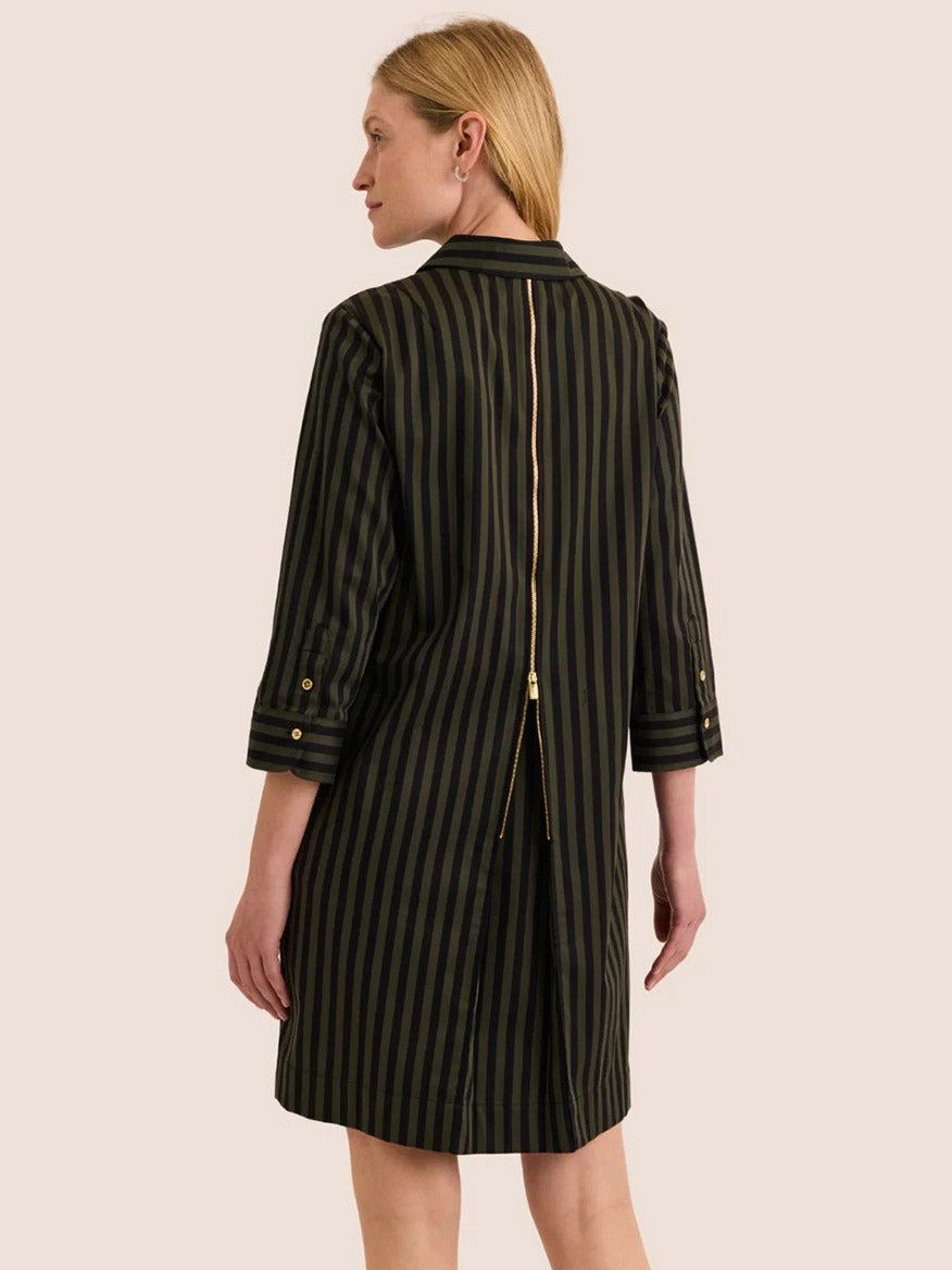 A woman stands facing away from the camera, wearing the Hinson Wu Alessa 3/4 Sleeve Classic Stripe Dress in Oregano/Black, crafted from premium cotton with vertical stripes and a visible gold zipper running down the back.