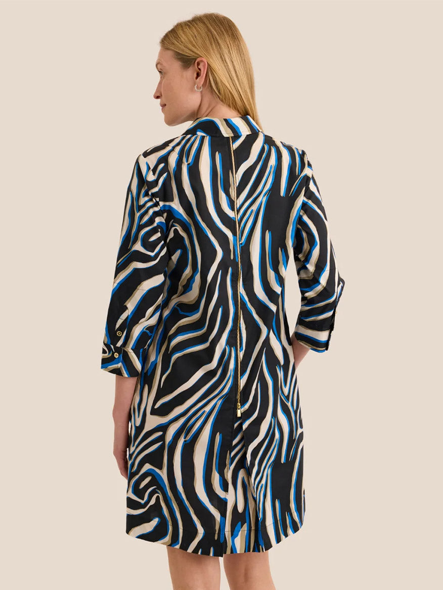 The model is seen from behind, wearing the Hinson Wu Alessa 3/4 Sleeve Abstract Zebra Dress—crafted from a premium cotton blend with exclusive black, white, and blue wavy zebra stripes—standing against a plain beige background.