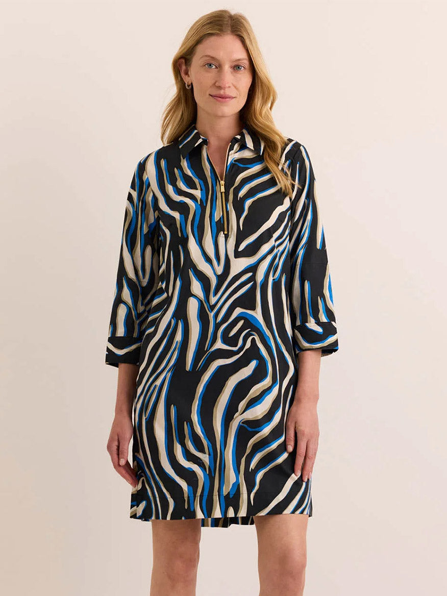 A woman stands against a plain background wearing the Hinson Wu Alessa 3/4 Sleeve Abstract Zebra Dress, a knee-length design made from a premium cotton blend with striking black, white, and blue zebra-inspired patterns and a short zip at the neckline.