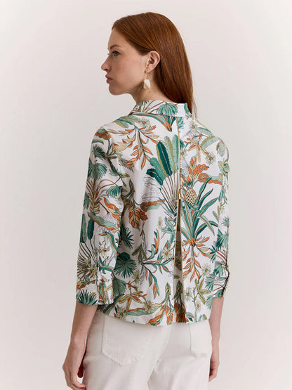 Woman with long red hair shown from the back wears the Hinson Wu Alessa 3/4 Sleeve Top in Amazonian Print, a white cotton blouse with green and orange exclusive patterns, paired with white pants against a plain background.