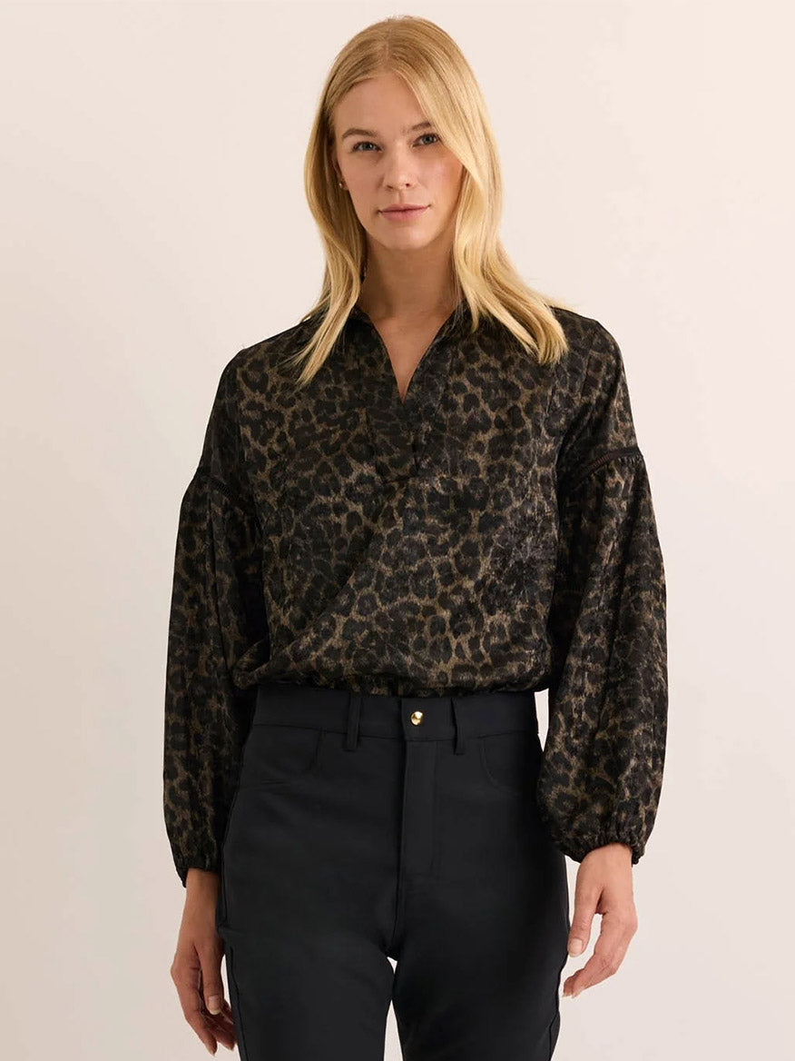 A woman wears the Hinson Wu Arianna Long Sleeve Animal Print Top in Animal Print, paired with black pants, standing against a plain, light background.