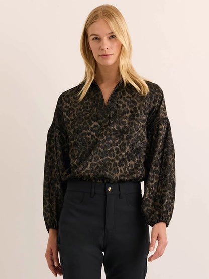 A woman wears the Hinson Wu Arianna Long Sleeve Animal Print Top in Animal Print, paired with black pants, standing against a plain, light background.