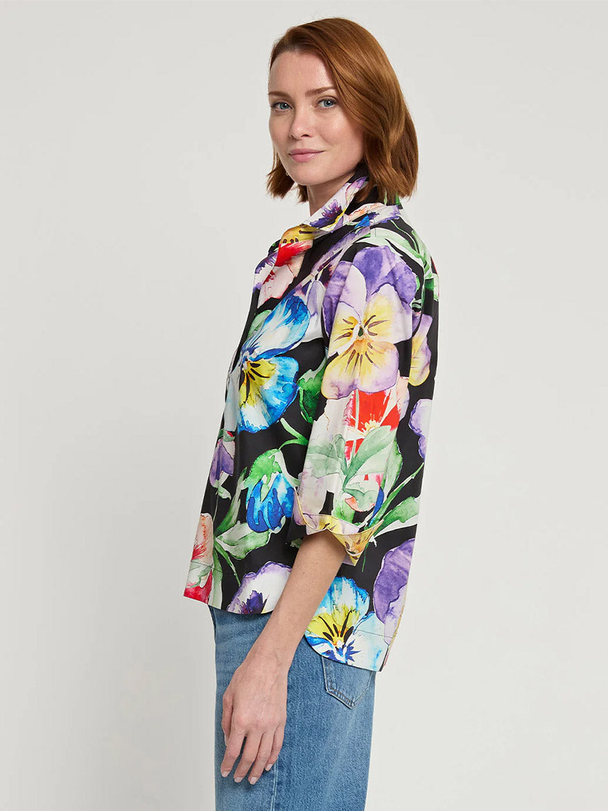 A person with short auburn hair, wearing the Hinson Wu Charlotte 3/4 Sleeve Pansy Print Top and blue jeans, stands in front of a plain background, turned slightly to the side.