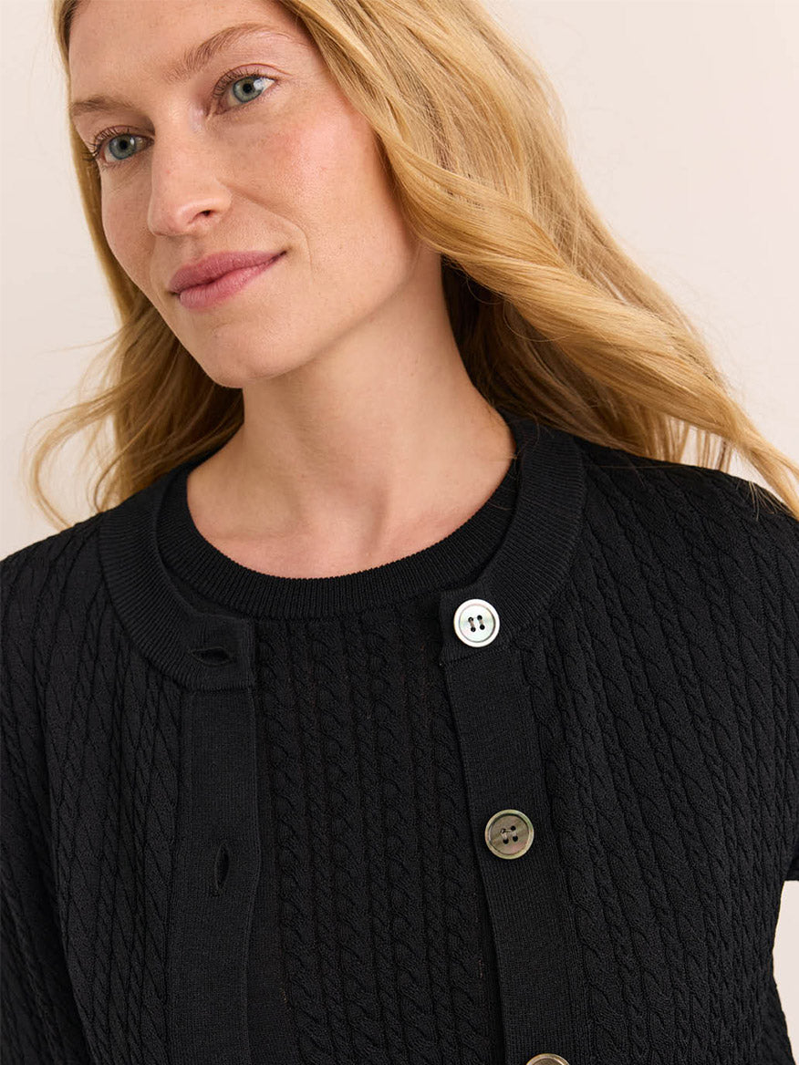 A woman with long blonde hair, wearing the Hinson Wu Edith Cardigan & Ashley Sleeveless Turtleneck Set in Black, gazes slightly to the side against a neutral background—her style exuding the timeless sophistication of an elegant dress.