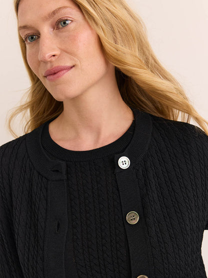 A woman with long blonde hair, wearing the Hinson Wu Edith Cardigan & Ashley Sleeveless Turtleneck Set in Black, gazes slightly to the side against a neutral background—her style exuding the timeless sophistication of an elegant dress.