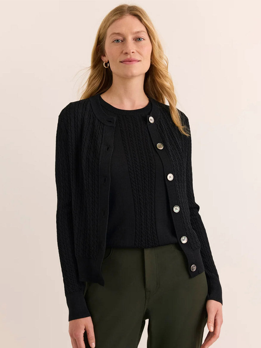 Wearing the Hinson Wu Edith Cardigan & Ashley Sleeveless Turtleneck Set in Black paired with olive green pants, a person stands against a neutral background, evoking the understated sophistication of an elegant dress.