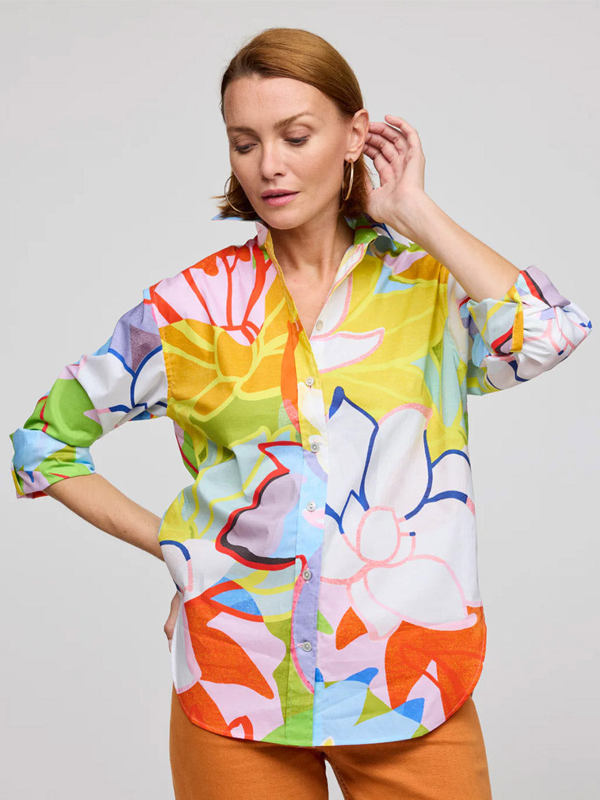 A woman wears the Hinson Wu Halsey Long Sleeve Lotus Print Shirt in Multi with orange pants, standing with one hand on her hip and the other touching her ear.