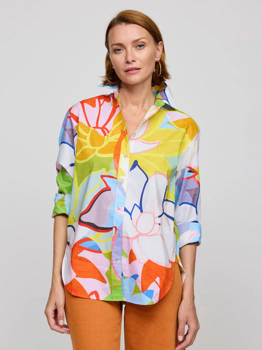 A woman wears the Hinson Wu Halsey Long Sleeve Lotus Print Shirt in Multi, a colorful oversized floral cotton shirt with exclusive prints and rolled-up sleeves, paired with orange pants against a plain light background.