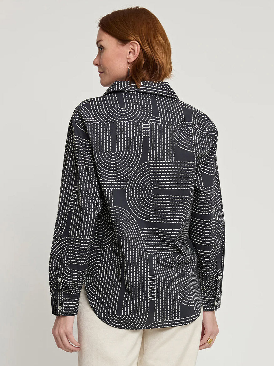 A person with short brown hair is wearing the Hinson Wu Halsey Long Sleeve Saddle Stitch Print Shirt, characterized by its black fabric adorned with a white dotted and line pattern. They are positioned slightly away from the camera, revealing the intricate details on the back of the shirt.