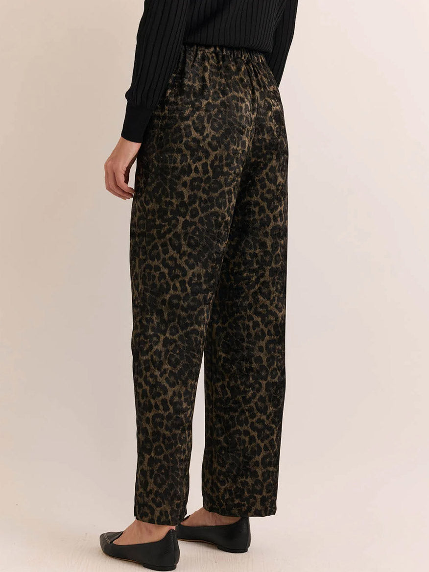 Wearing the Hinson Wu Hostess Animal Print Pant in Animal Print featuring a relaxed straight leg and brushed textured finish, paired with a black long-sleeve top and black flats, this person is shown from the back against a plain background.