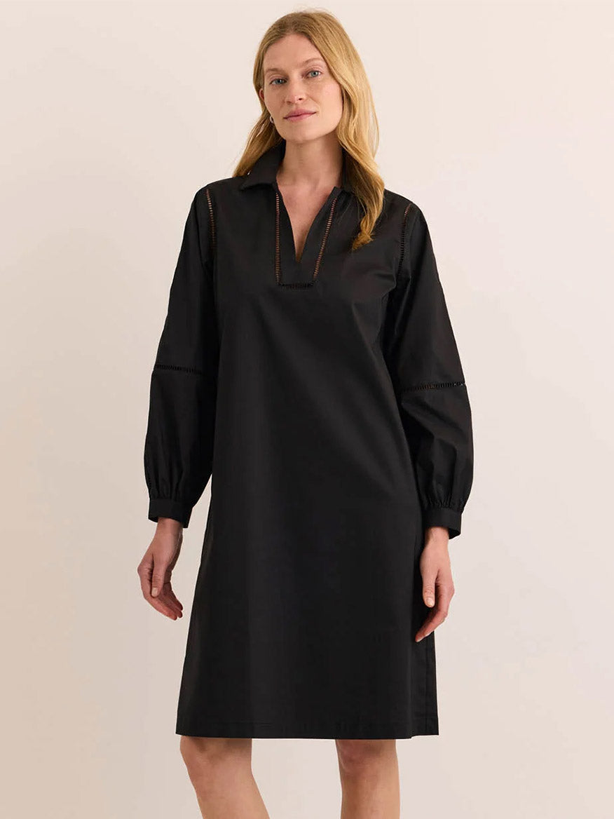 Wearing the Hinson Wu Laura Long Sleeve Lace Trim Dress in Black, this woman stands against a plain light-colored background. The dress features a collar, V-neckline, and is crafted from a refined blend fabric for a relaxed fit.