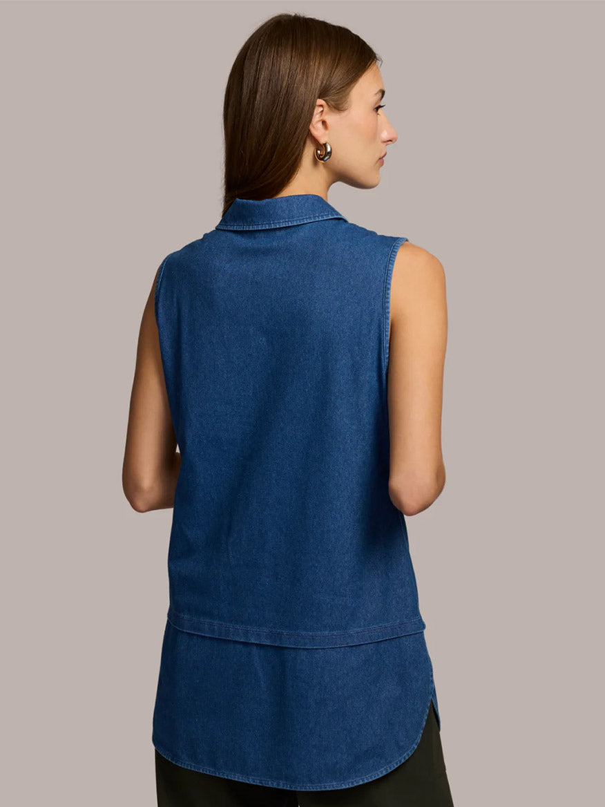 A woman with straight brown hair is seen from the back, wearing the Hinson Wu Lea Sleeveless Knit Denim Foundation Layer in Medium Wash, combining style and comfort against a plain beige background.