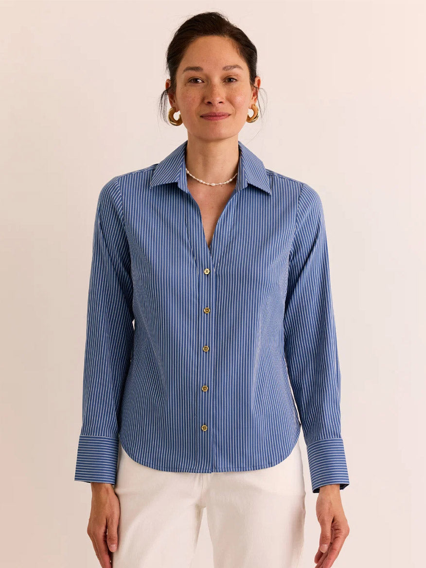 A woman stands against a plain light background wearing the Hinson Wu Lindsey Long Sleeve Ribbon Stripe Shirt in Blue/White Stripe paired with white pants.