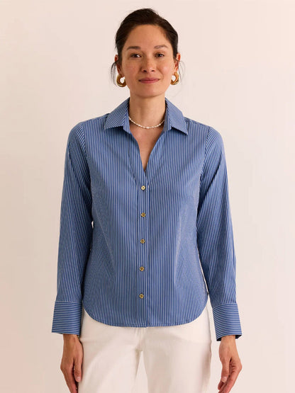 A woman stands against a plain light background wearing the Hinson Wu Lindsey Long Sleeve Ribbon Stripe Shirt in Blue/White Stripe paired with white pants.